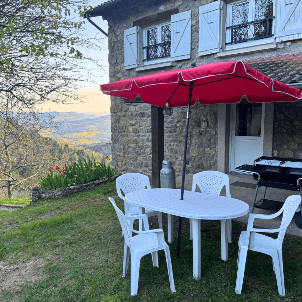 table et chaises de jardin avec parasol rouge du gite pourette, en plein milieu du jardin fleuri