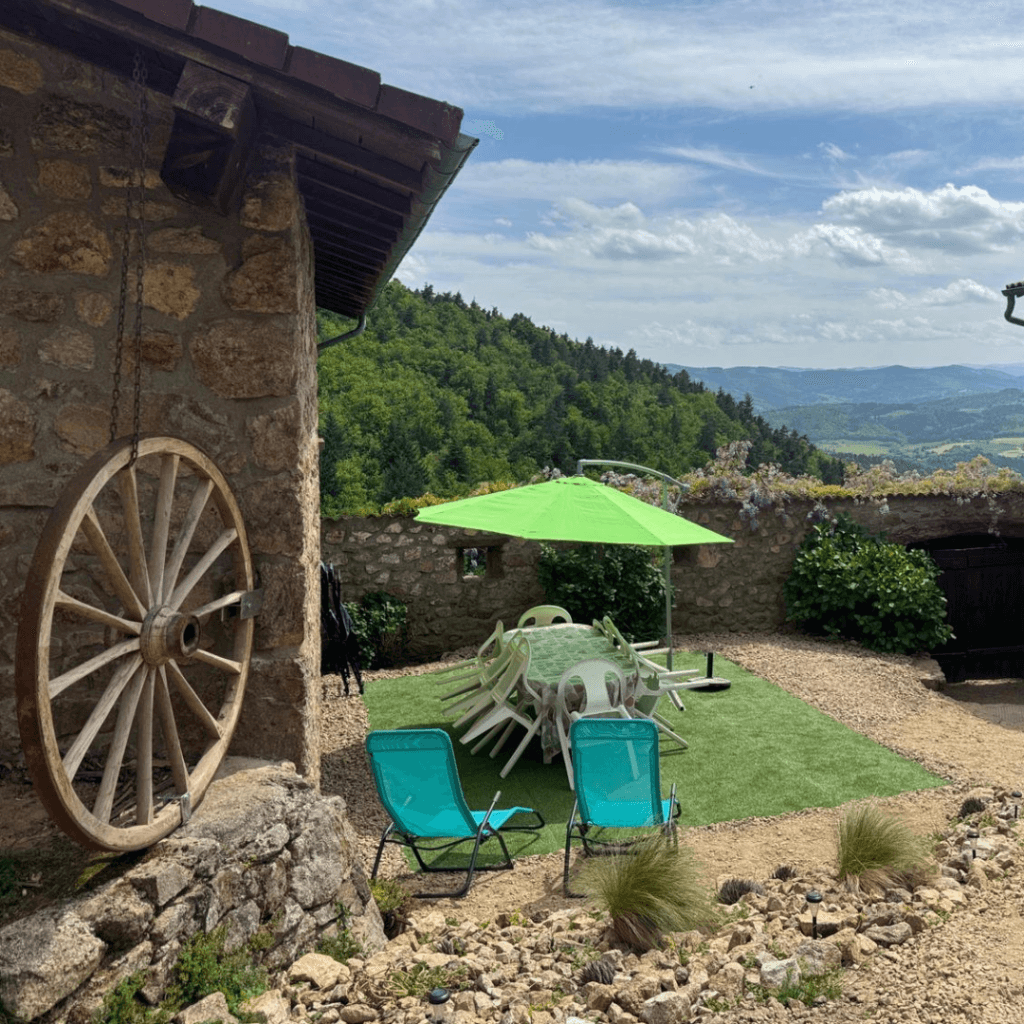 gite lamastre ardeche- terrasse du gite la comballe avec une table des chaises, un parasol vert et des transats sur une fausse pelouse