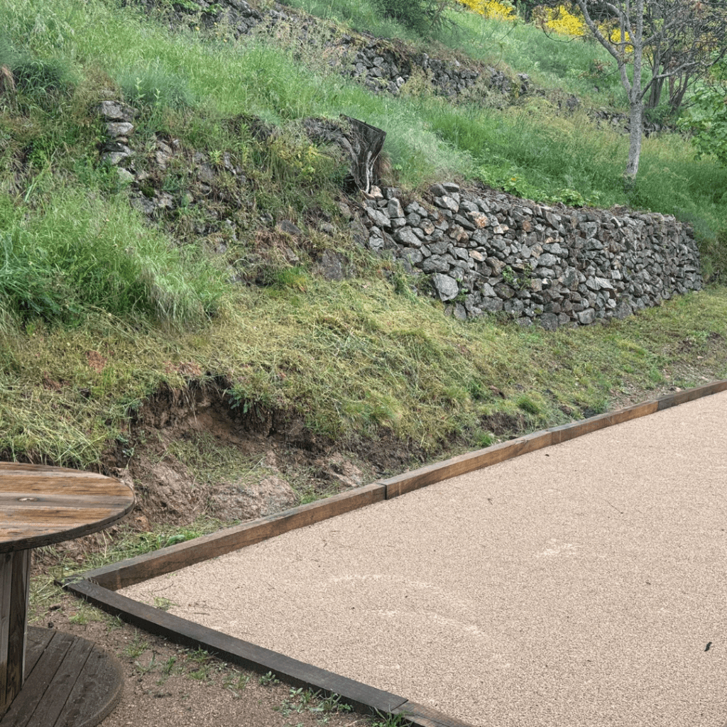 terrain de pétanque entouré de verdure avec une table ronde en bois