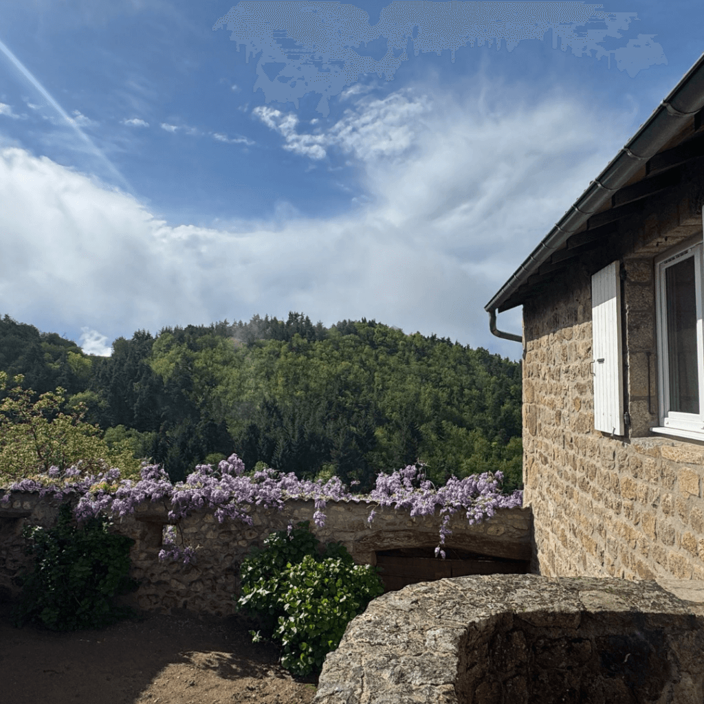 vue sur le grand gite de la Comballe avec un mur en pierre et fleurs violettes